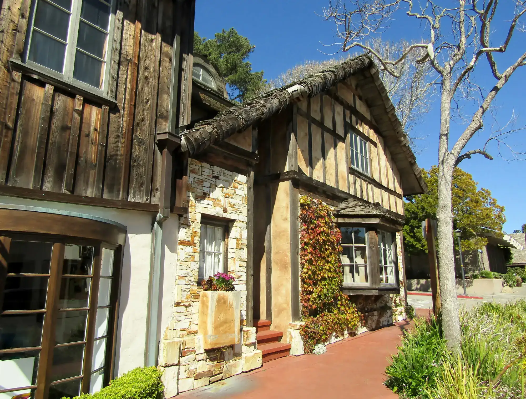Half tiered house with a bay window, night stone on the left of the entrance, dead tree on the right, on a sunny day in Carmel-by-the-Sea, while on a Big Sur road trip.