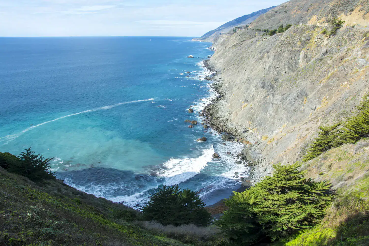 Looking down a green cliff on the blue water on the trail to Ragged Point during a road trip from LA to Big Sur.