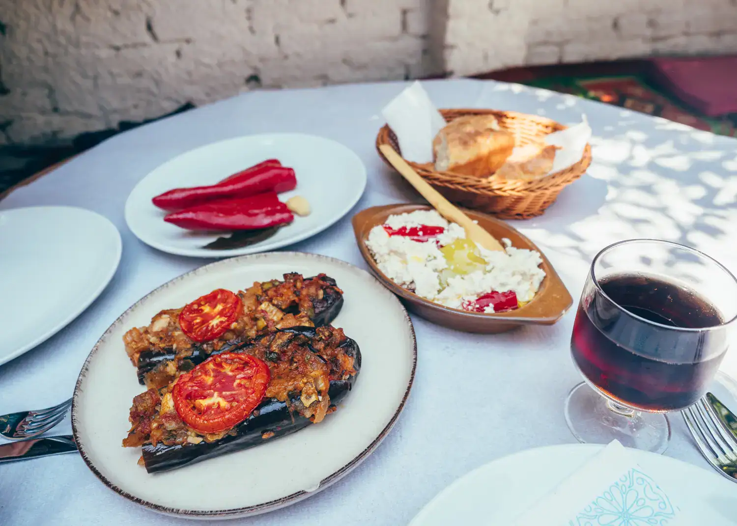 Round white table with white plates with gratinated eggplant, paprika, cheese with peppers, a glass of coke and a bread basket at Oda, one of the best restaurant in Tirana.