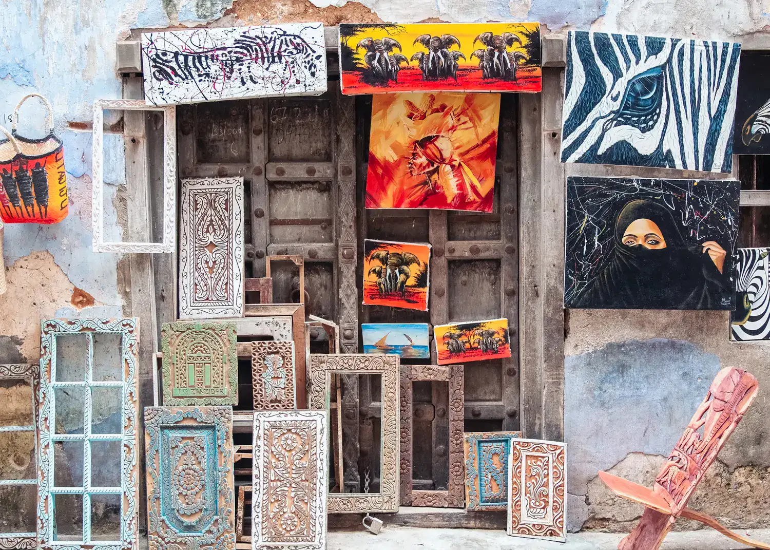 Shop in front of two old wooden doors selling paintings and intricately carved wooden frames, in Stone Town Zanzibar.