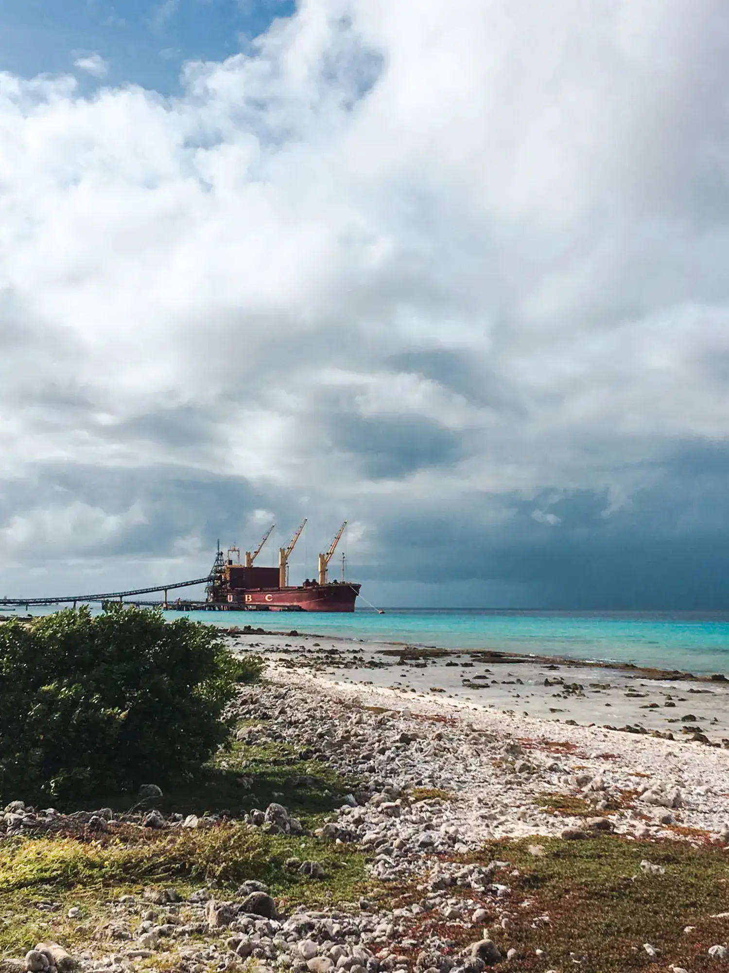 Ship aground in turquoise ocean on a stony beach on a cloudy day in Bonaire.