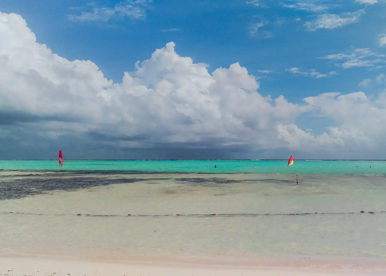 Wind surfers in shallow turquoise water under white clouds on a sunny day in Bonaire, from a cruise ship.