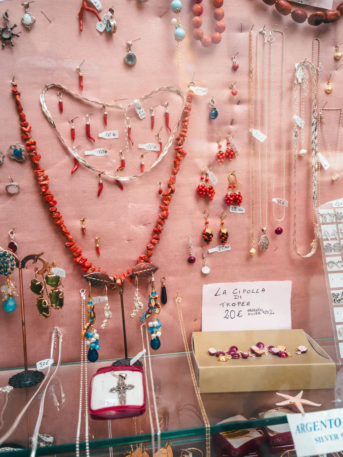 Light pink wall with charms (chilis and red onions) and necklaces for sale in Tropea, Italy.