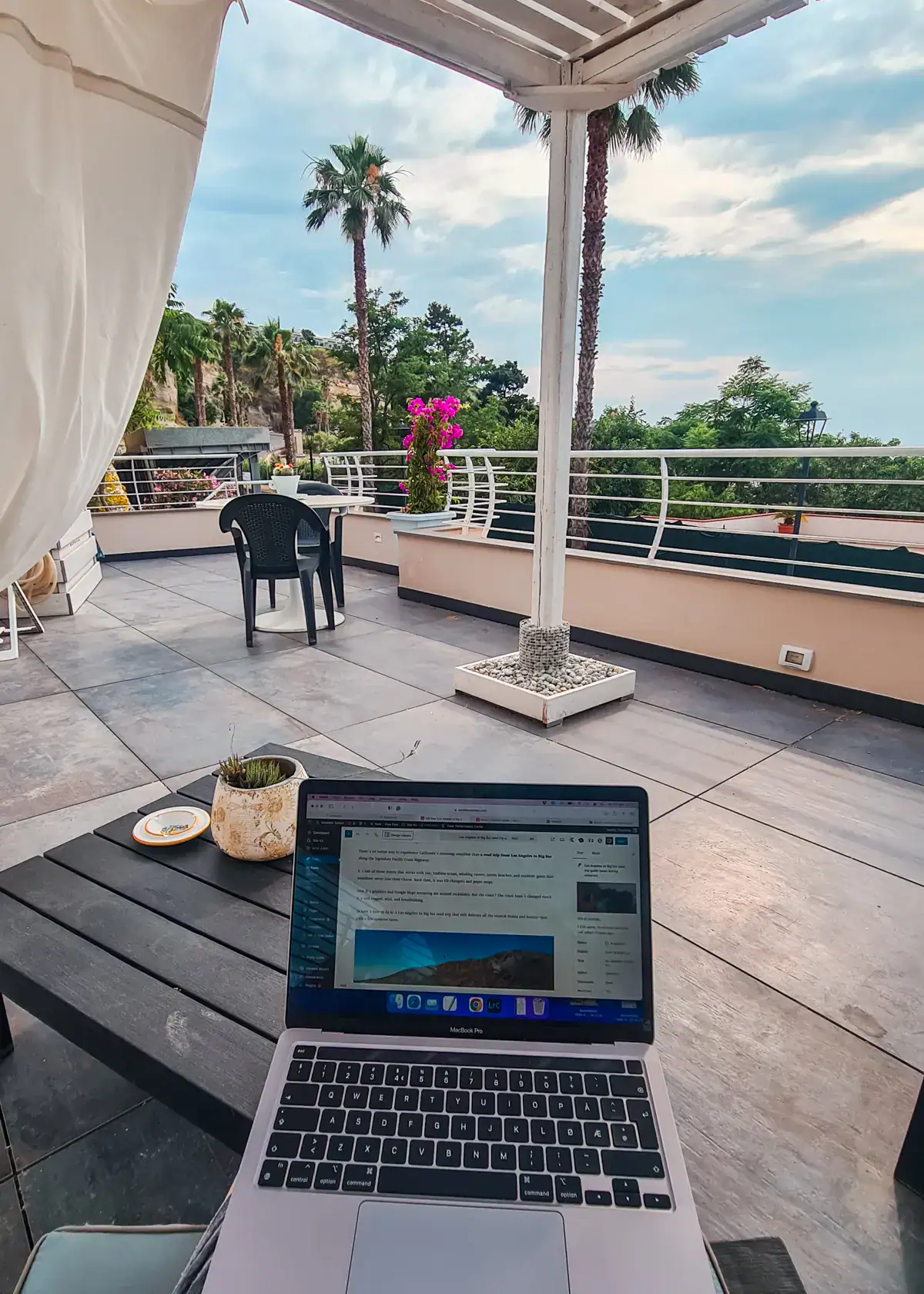 Laptop on my lap, looking out over the tiled rooftop of H2O TROPEA, greenery and skinny palm trees in the background, one of the best places to stay in Tropea.