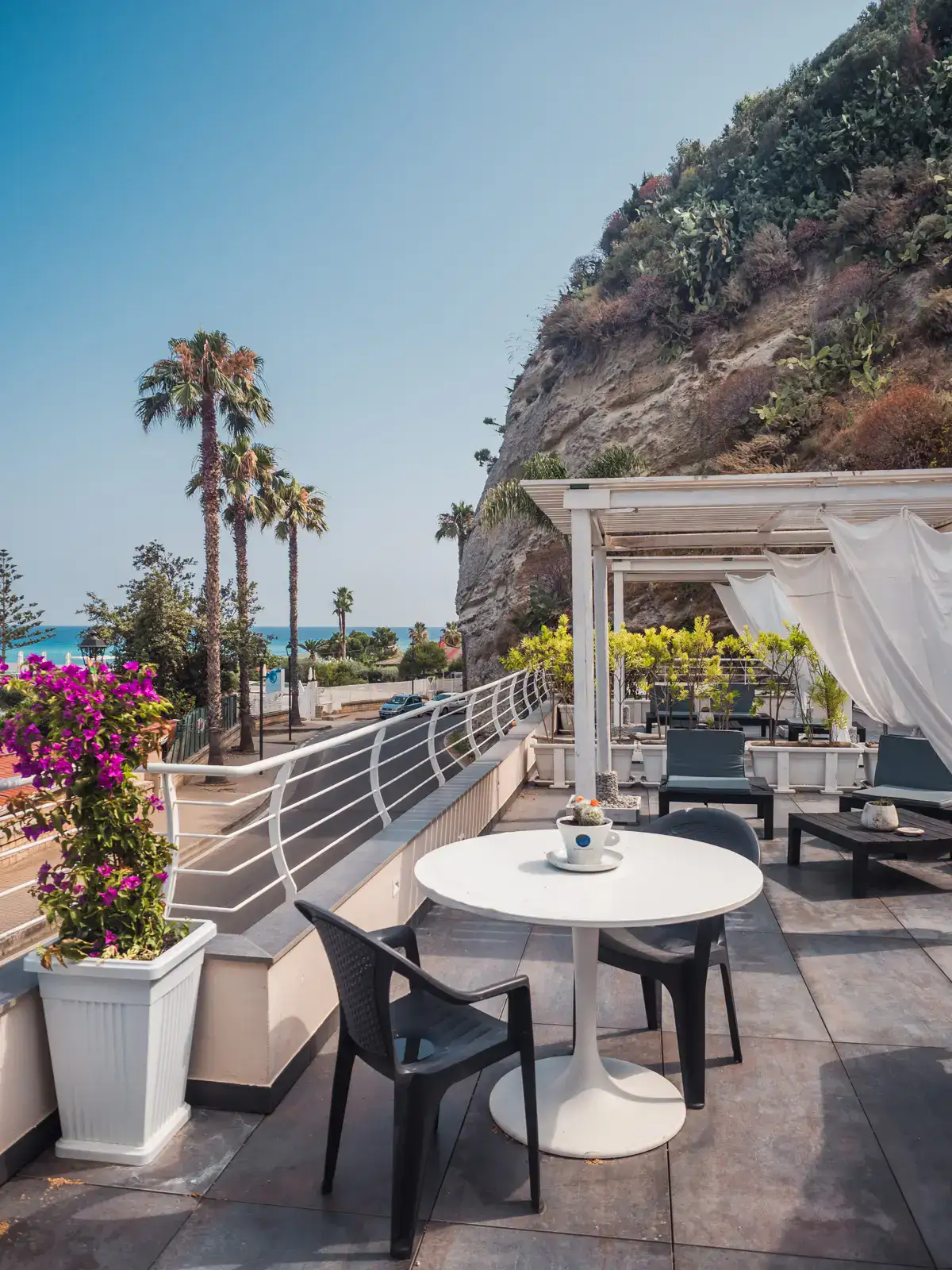 Rooftop at H2O TROPEA with a white cabana with white curtains, white round table with black chairs, skinny palm trees in the background, one of the best places to stay in Tropea.