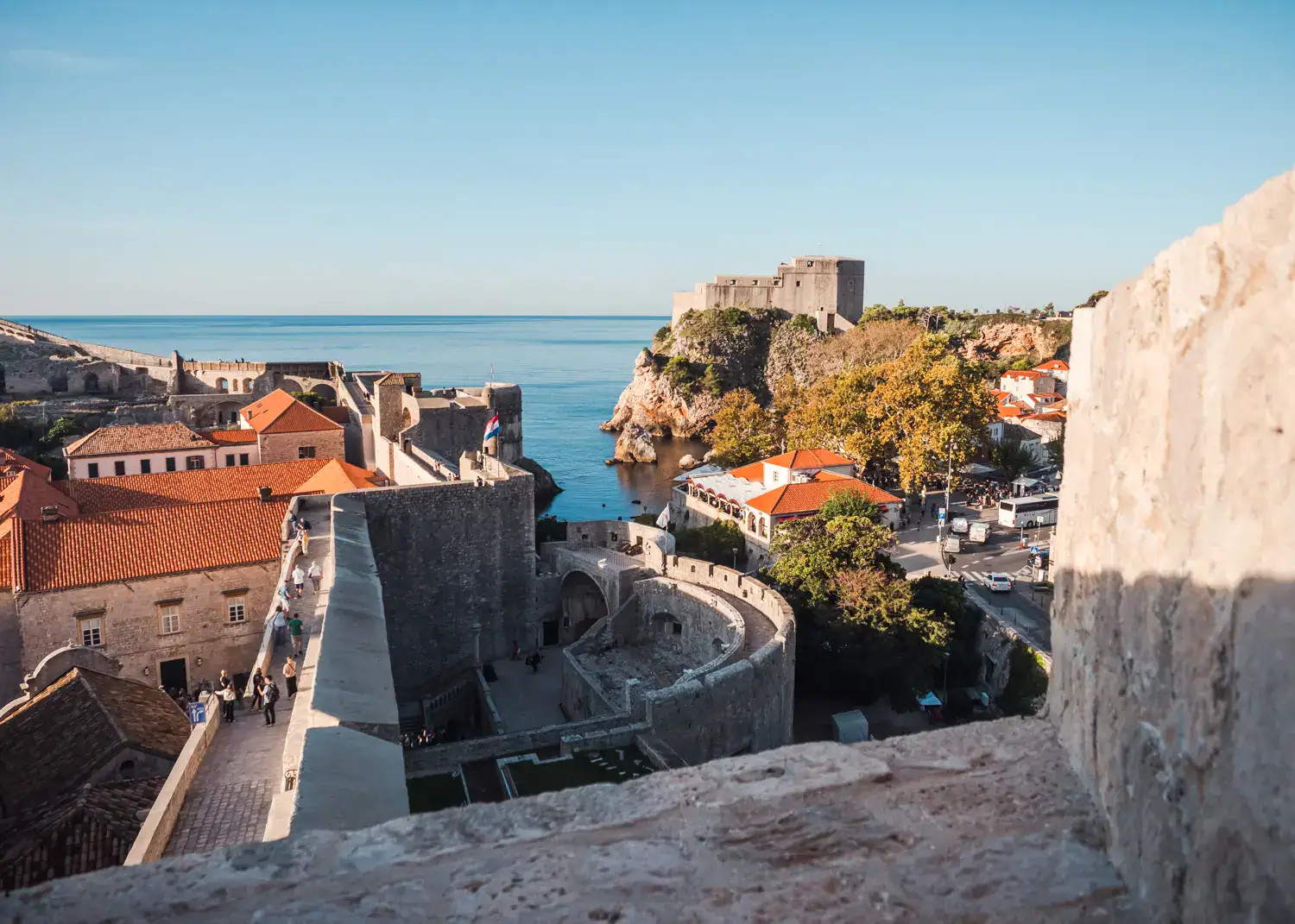View of orange rooftops in Dubrovnik Old town, the ocean and Fort Lovrijenac on a green hill, seen fro the Old Town Walls, Dubrovnik is the one the best European cities to visit in October.