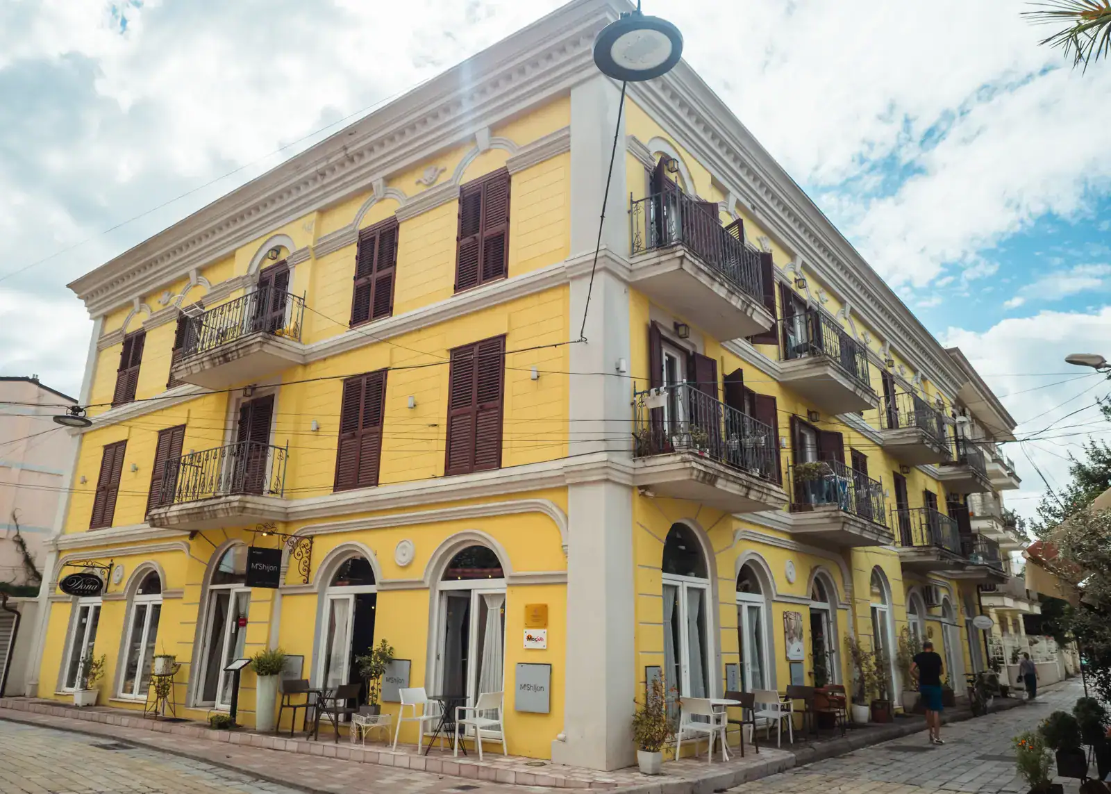 Grand, old yellow building, with white trims, brown shutters and arched windows on the first floor, Arti Zanave one of the best restaurants and charities in Shkoder.