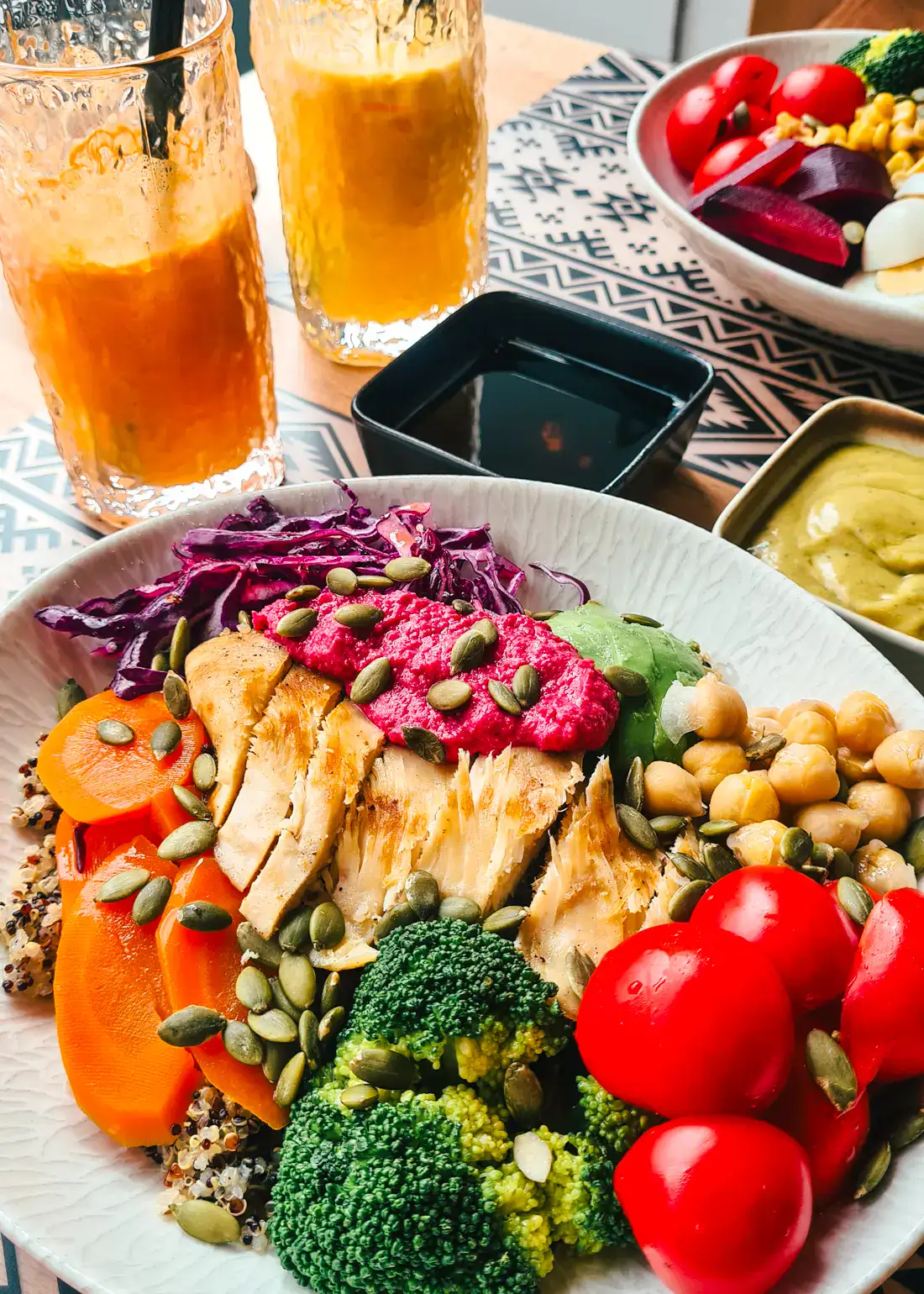 Bowl of colorful vegetables and chicken with beetroot hummus, cherry tomatoes, broccoli, chickpeas, carrots and seed, orange juice in the background at Kuzin Restaurant in Shkoder, Albania.