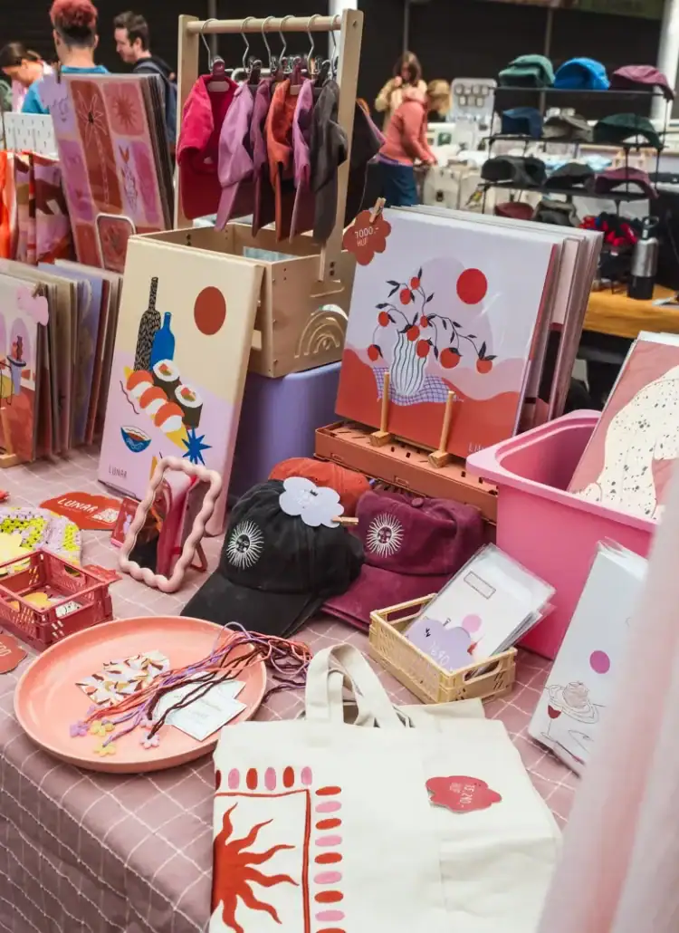 Tables displaying totes, scarfs prints at hats in pink, purple and orange colors at the Makers' Market in Budapest.