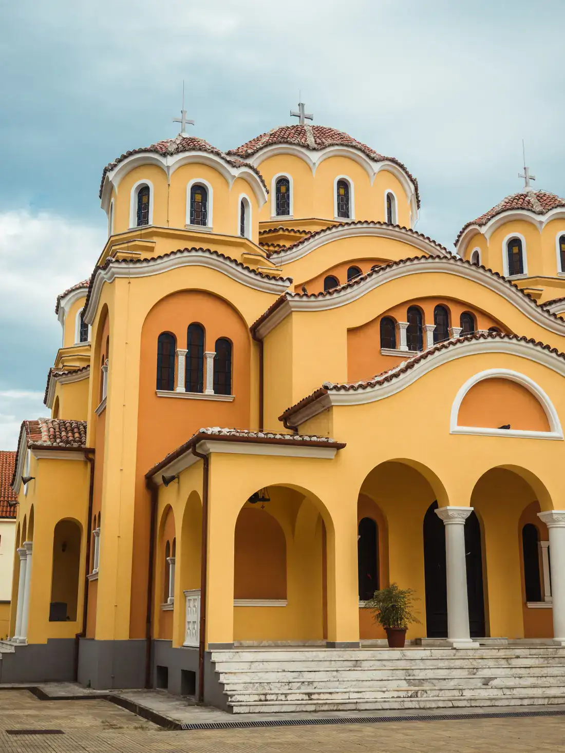 Yellow and orange, Orthodox Church with three domes with crosses on top, on a clouded afternoon in Shkoder, Albania.
