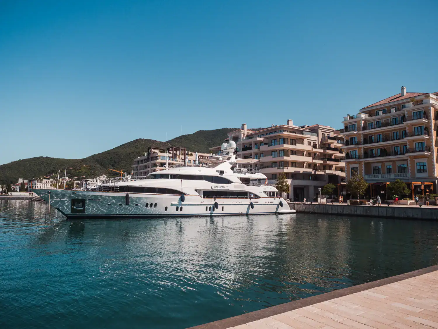 White yacht at Porto Montenegro on a sunny day with clear, blue skies. Large, light yellow buildings in the background. Is Tivat worth visiting?