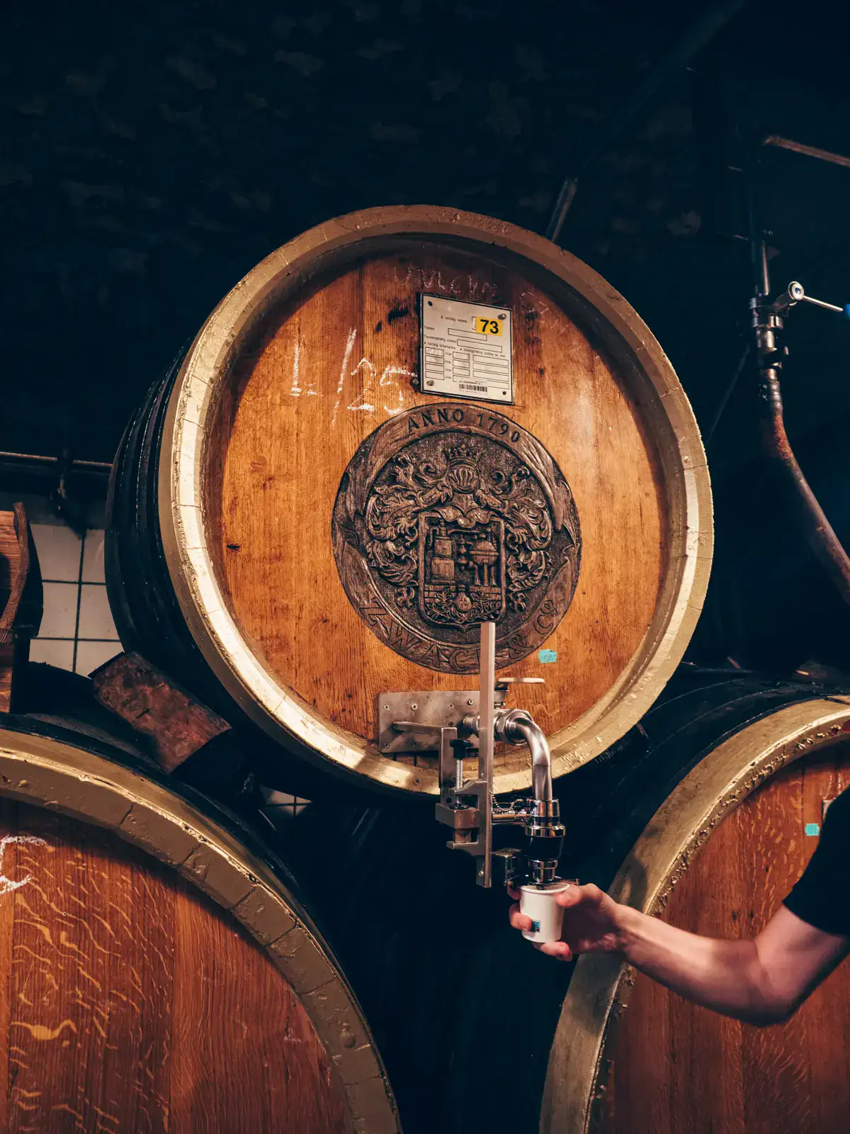 Our guide, tapping Unicum shot from a wooden barrel with the Unicum logo during a premium tour of the Factory and Museum in Budapest.