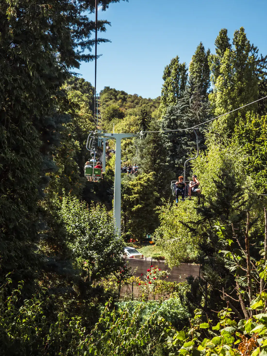Siting on Zugliget Chairlift going through lush, green forest just outside Budapest, on a sunny day.