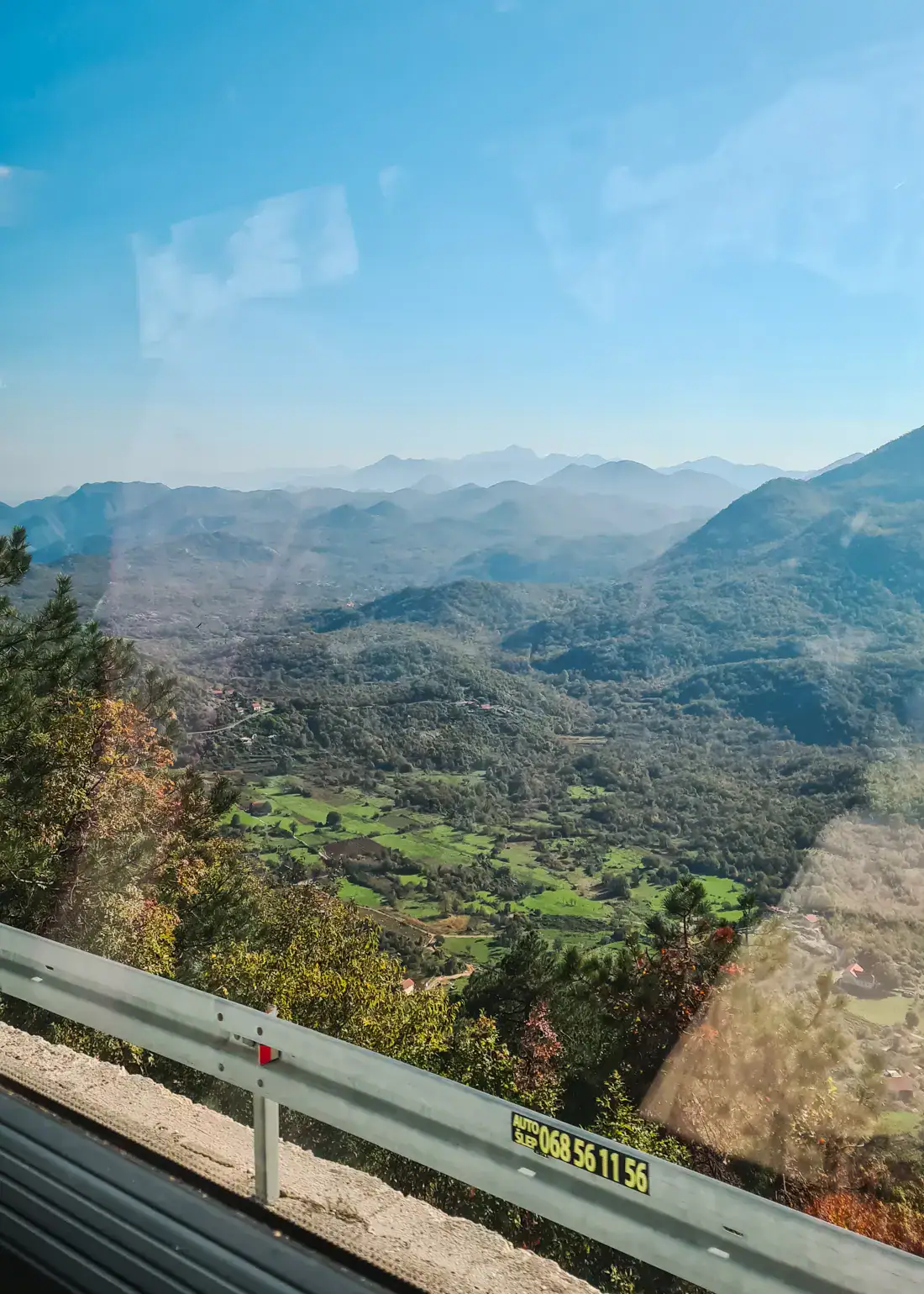 View out a bus window of a lush valley with mountains in the background on a sunny day with blue skies, traveling from Budva to Tirana.