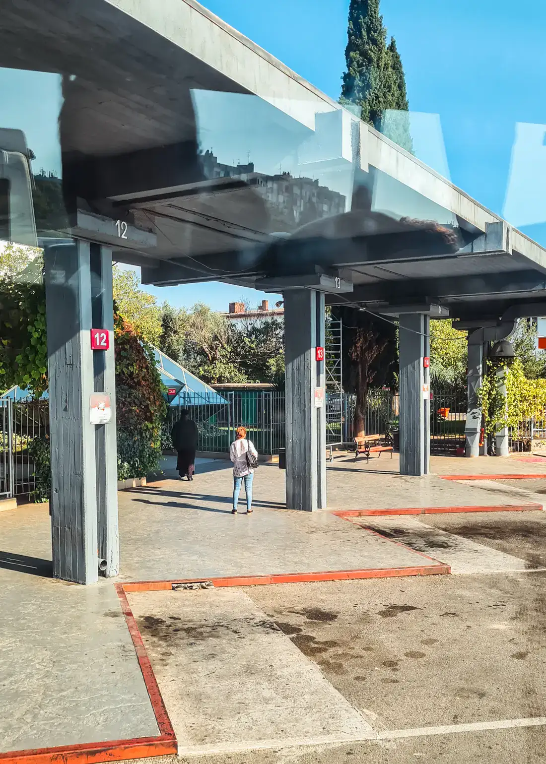 Man standing between two concrete columns on a sunny day at Podgorica bus station, one the way from Budva to Tirana by bus.