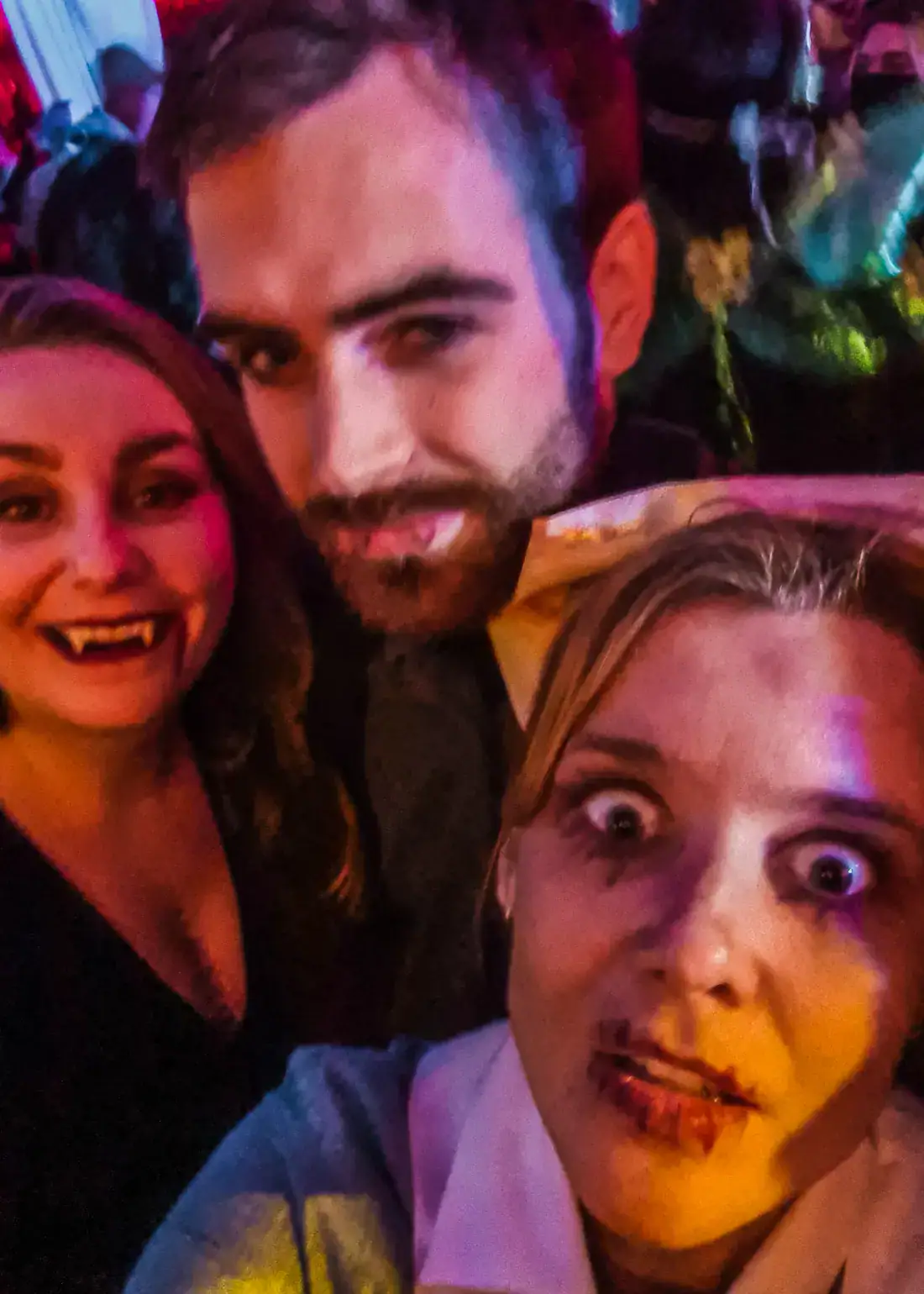 Woman with long hair, smiling with vampire teeth, man in the middle with dark hair and beard and woman as a dead nurse in old uniform looking with crazy eyes into the camera, at the Bran Castle Halloween Party.