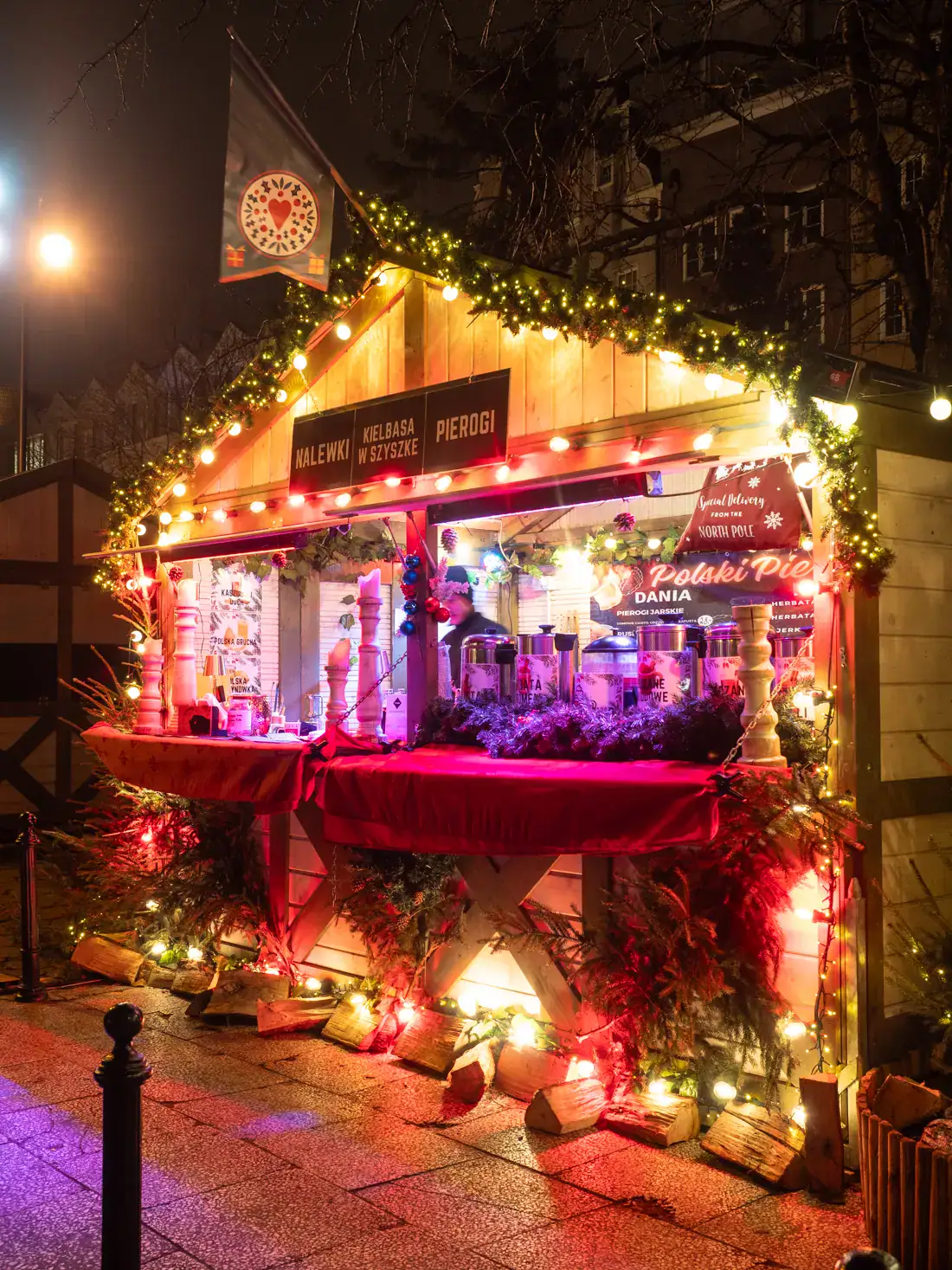 Wood stall selling mulled wine, decorated in garland, red table cloths and colorful lights, glowing at Gdansk Christmas Market.