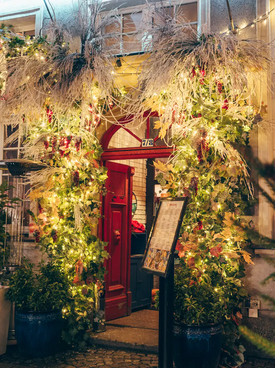 Open red door with an arched window above, decorated with greenery, straw, grapes and lights around in Gdansk for Christmas.