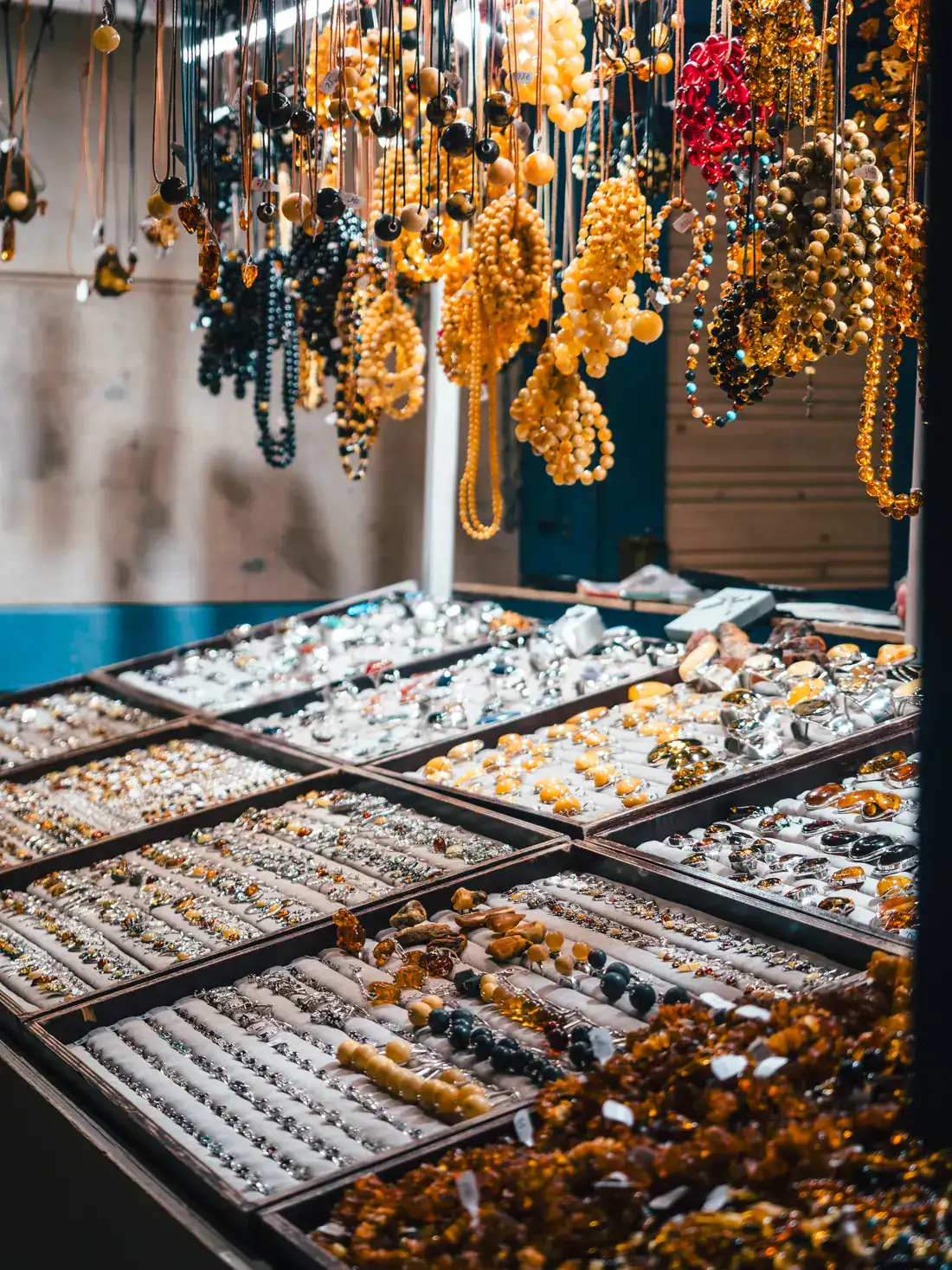 Looking into a stall at Gdansk Christmas Market with treys of amber jewelry, half white and blue wall in the background, and orange and darker amber jewelry hanging from the ceiling.