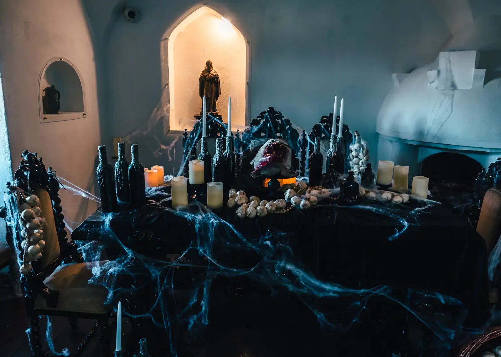 Table inside Bran Castle with bottles, candles, garlic, cobweb and a scary mask, surrounded by white stone walls, during the special Halloween tour.