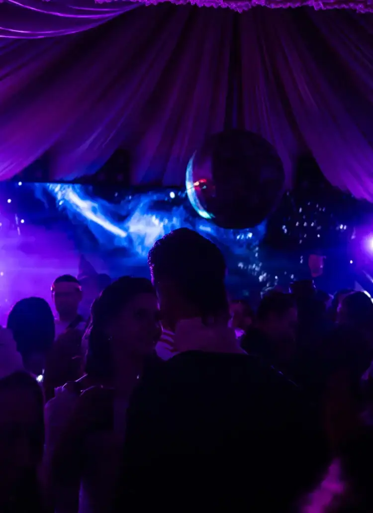 Couple looking at each other, surrounded by people in costumes, inside a dark, large tent with blue and purple lights, at the Halloween party at Bran Castle in Transylvania, Romania.