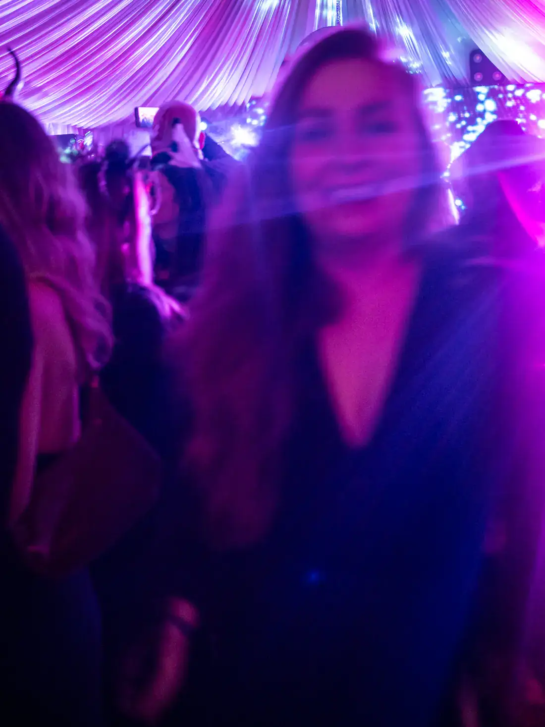 Blurry woman with long hair in a black dress, smiling in the purple light inside a large tent at the Bran Castle Halloween Party.