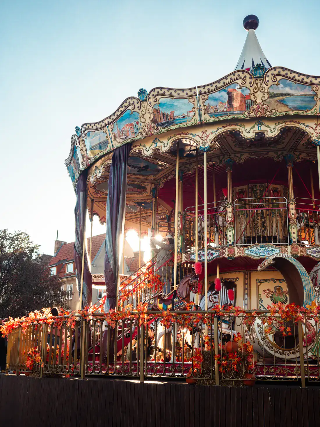 Close up of an ornate carousel, gold and red with colorful paintings, decorated with orange fall leaves, in the Old Town, one of the best places to stay in Gdansk.