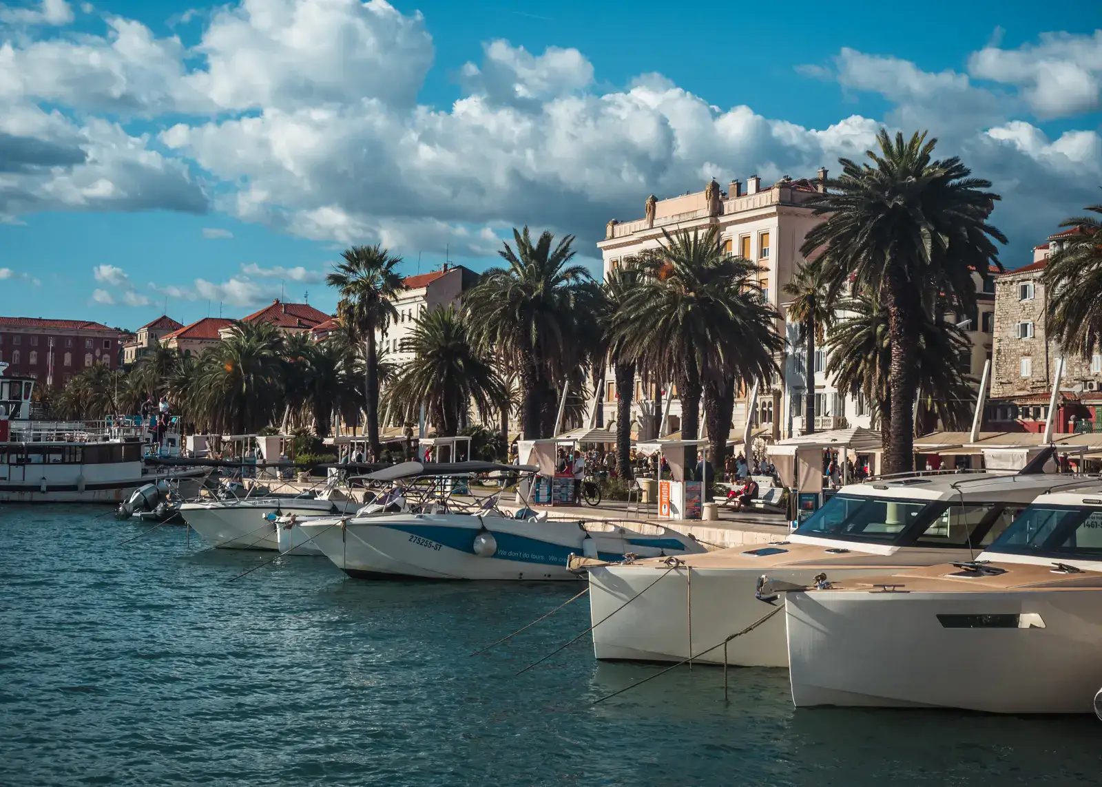 Private boats docked along the waterfront promenade in Split Old Town lined by large palm trees on a sunny day with some clouds. Is Split worth visiting?