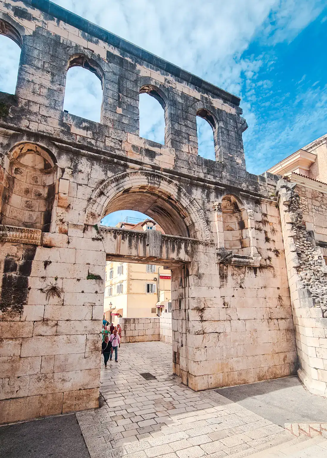 Tall sandstone gate with some black discoloration and an arched opening and arched windows above inside Split Old Town, the highlight of visiting.