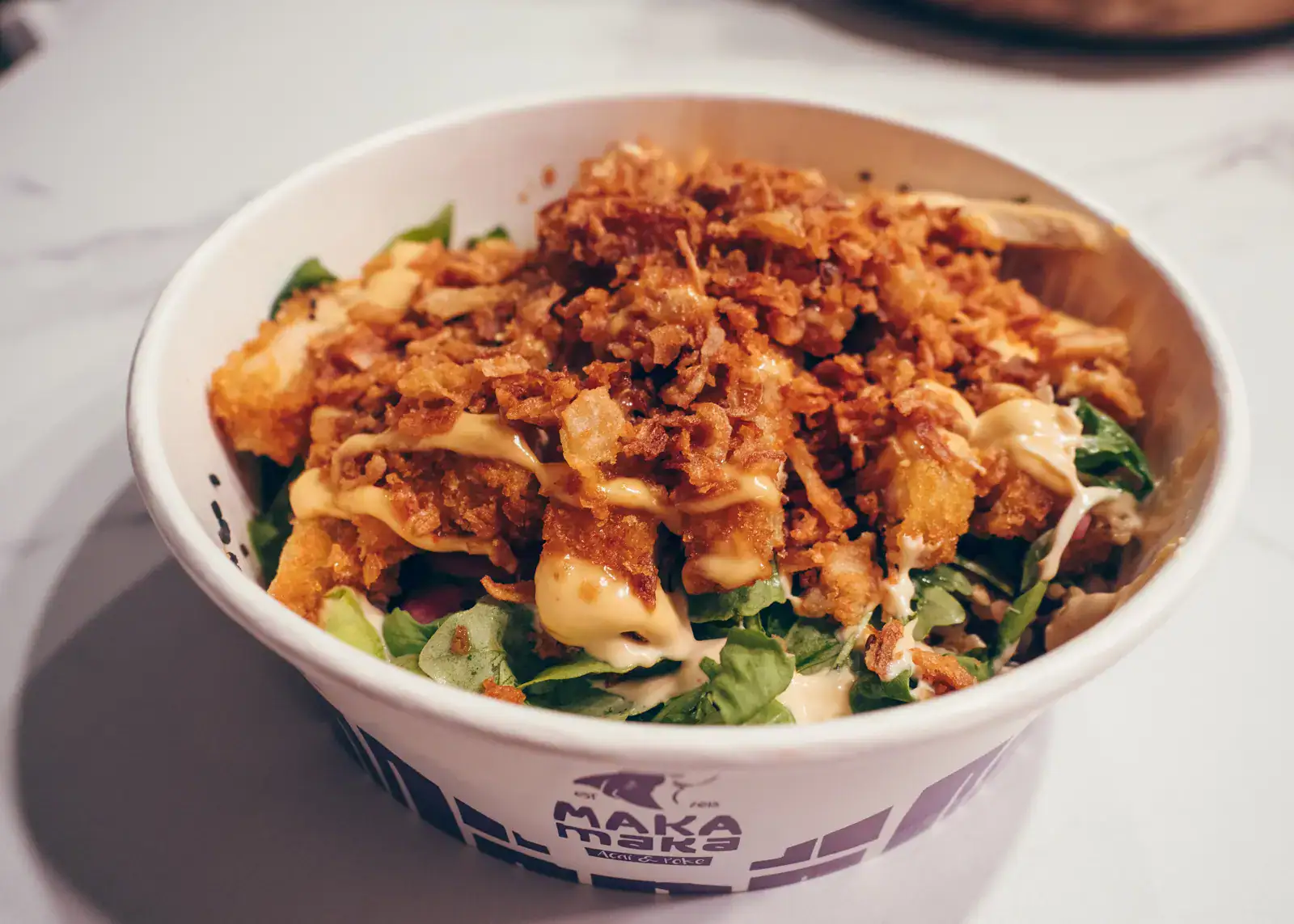 White paper bowl with purple text from Maka Maka with crispy chichek salad, one of the best restaurants in Split.