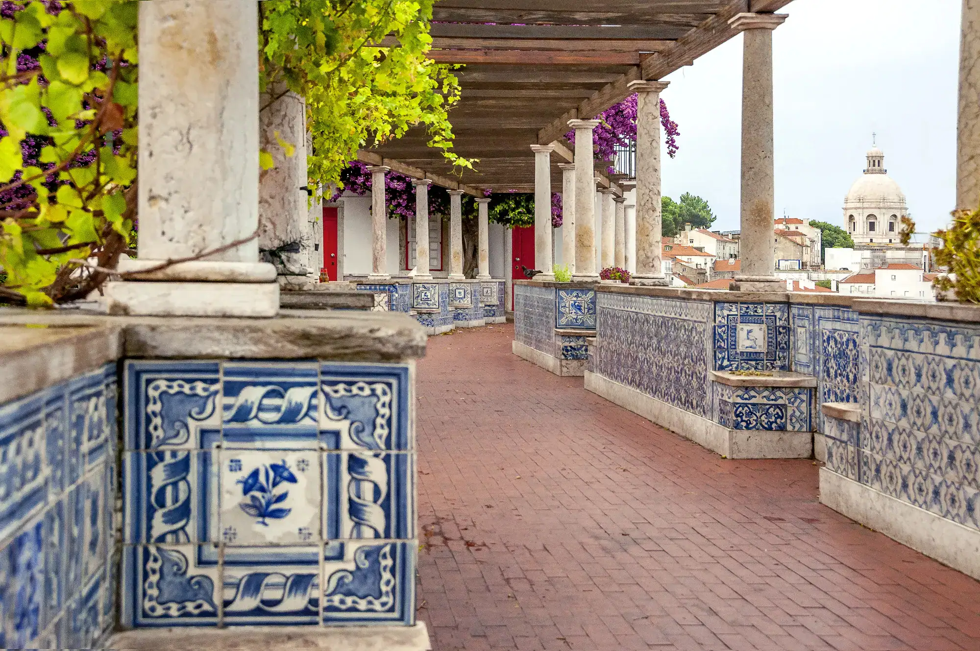 View of Miradouro de Santa Luzia with terracotta tiles on the floor and white and blue tiles along the walls, columns holding the roof, a must during your one day in Lisbon.