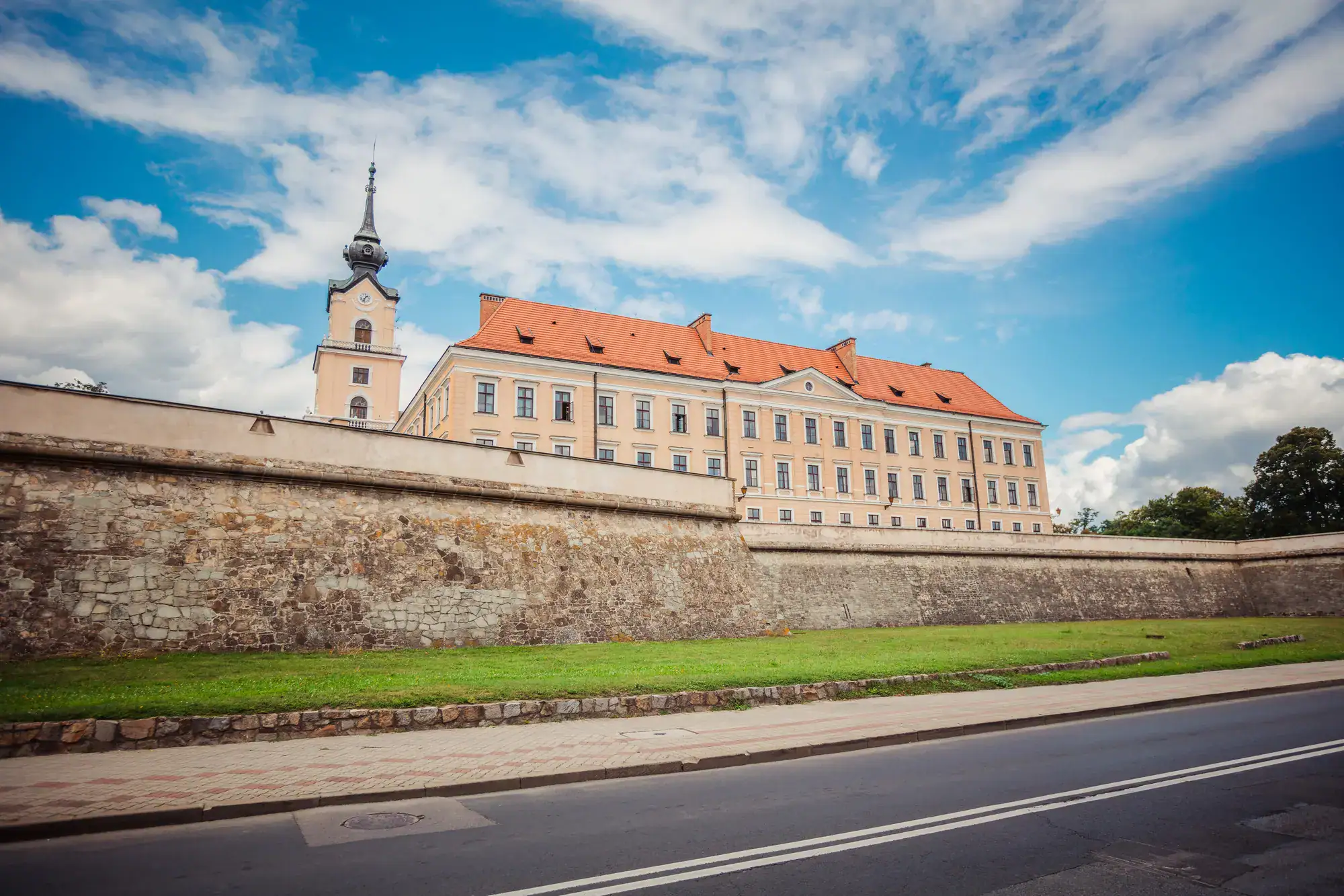 View from the road of the yellow Rzesz&oacute;w Castle, with a turret and orange roof, and 3 rows of 20+ windows, built up on a wall, seen on a day trip from Krakow.