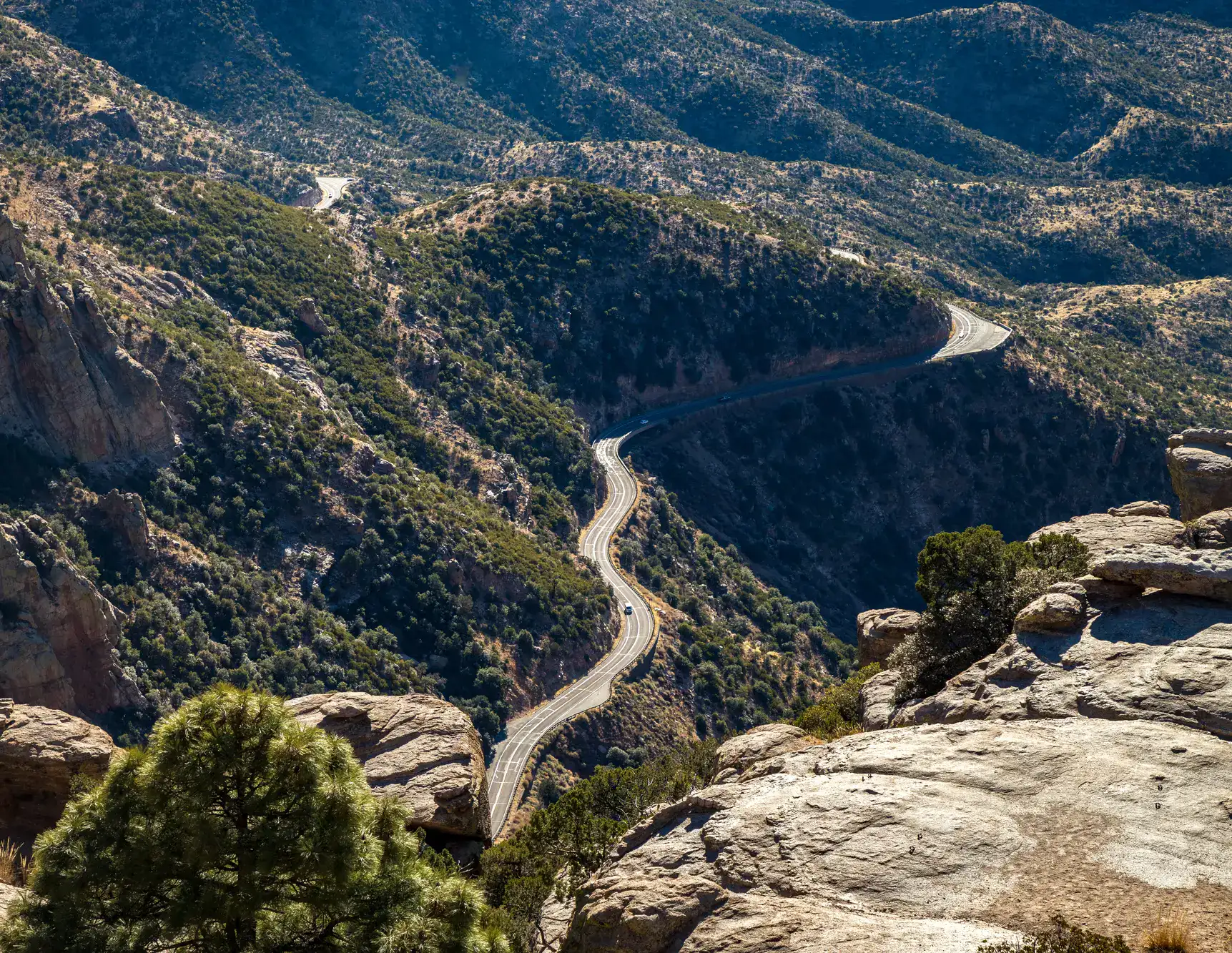 Looking down on the Mount Lemmon Scenic Byway running through mountainous landscape covered in green bushes and shrubs from a cliff on a sunny day, one of the top things to do in Tucson.