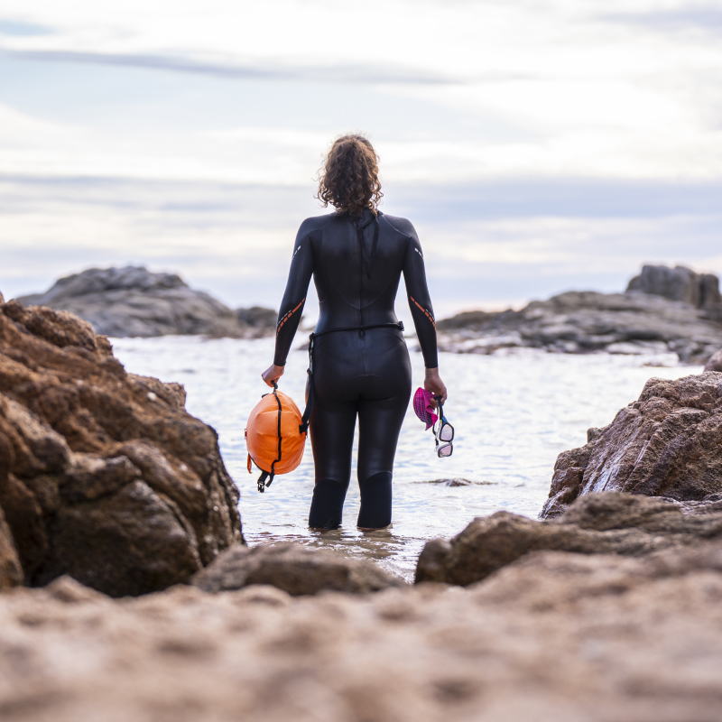 En kvindelig atlet, der er svømmer, står ansigt til ansigt med havet iført konkurrencedragt