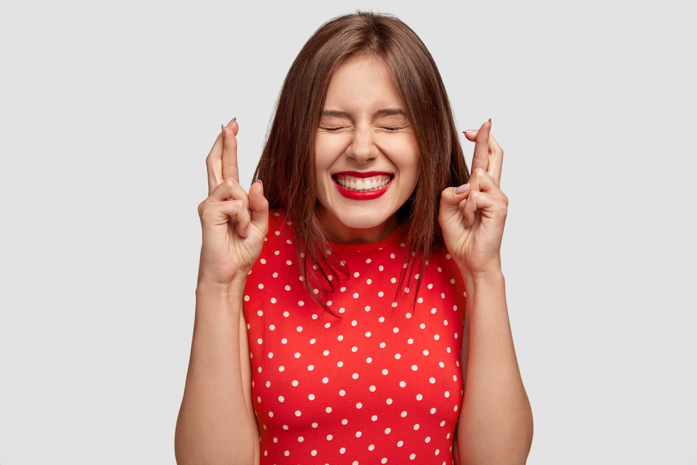 A woman crosses her fingers with an excited expression on her face.