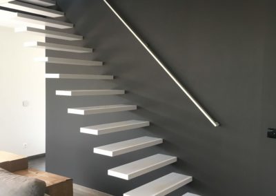 Antraciet muur in woonkamer met witte zwevende trap en witte trapleuning