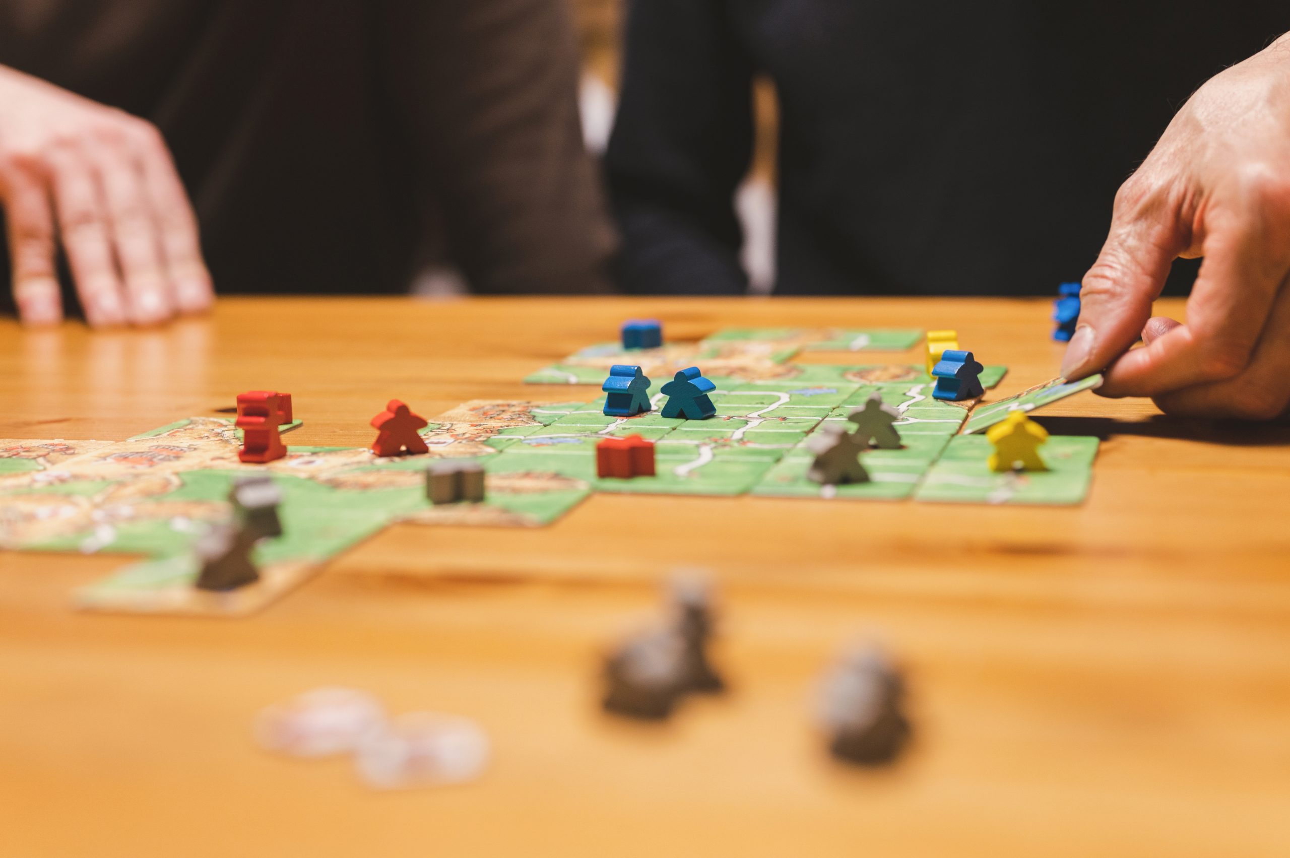 Players placing colorful game pieces on a green tile board with grid paths and buildings