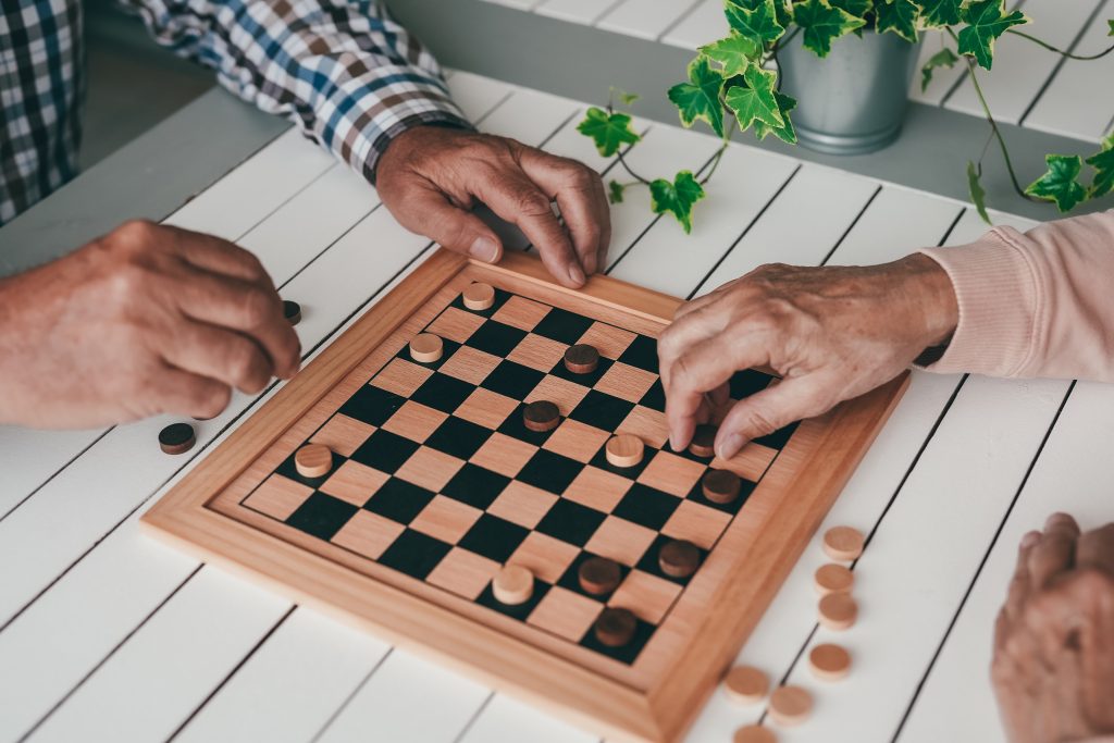 Two people playing checkers on a wooden board with black and white round pieces