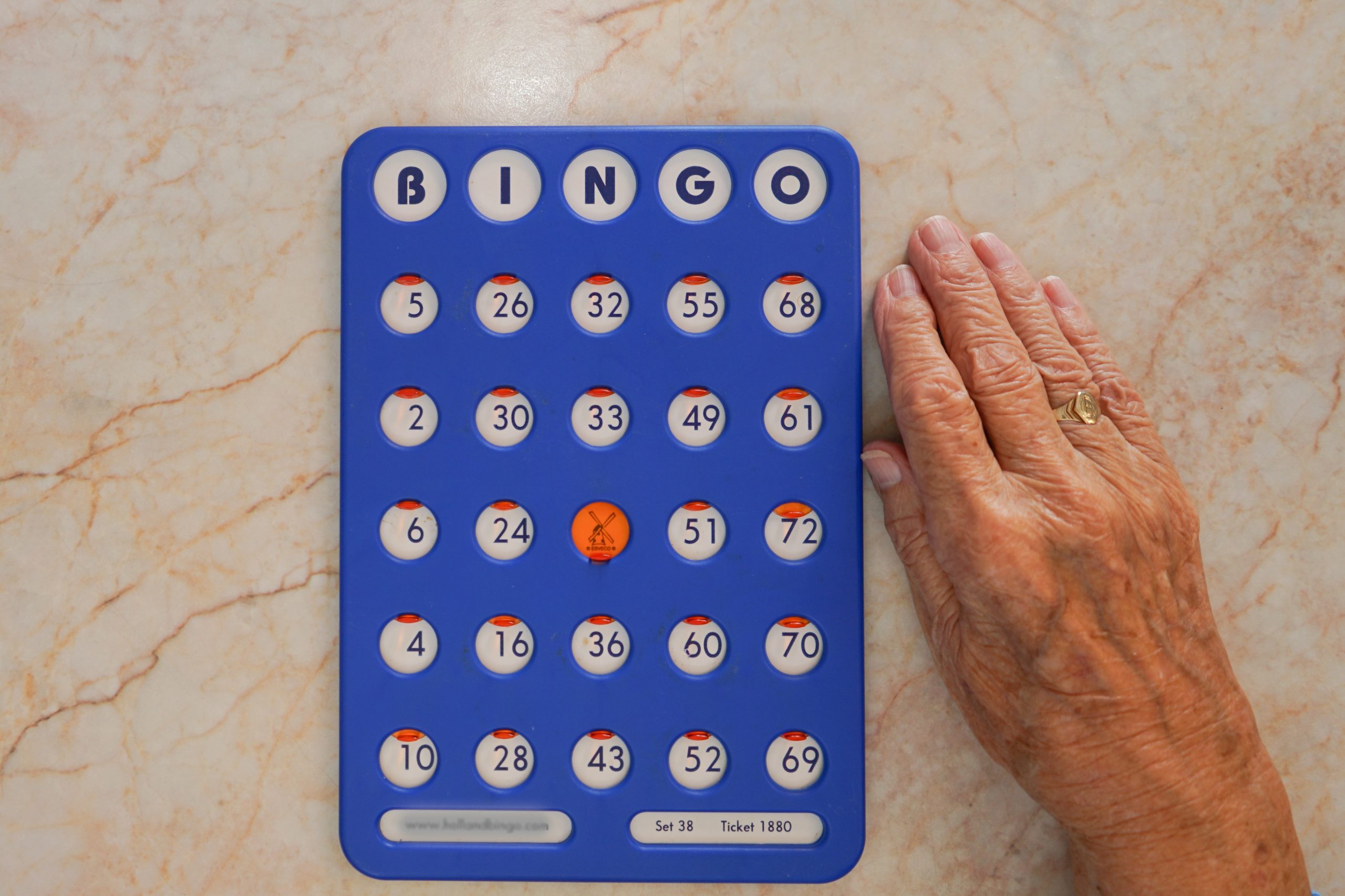 Bingo card with numbered slots and one marker in the center, beside an elderly person's hand on a table