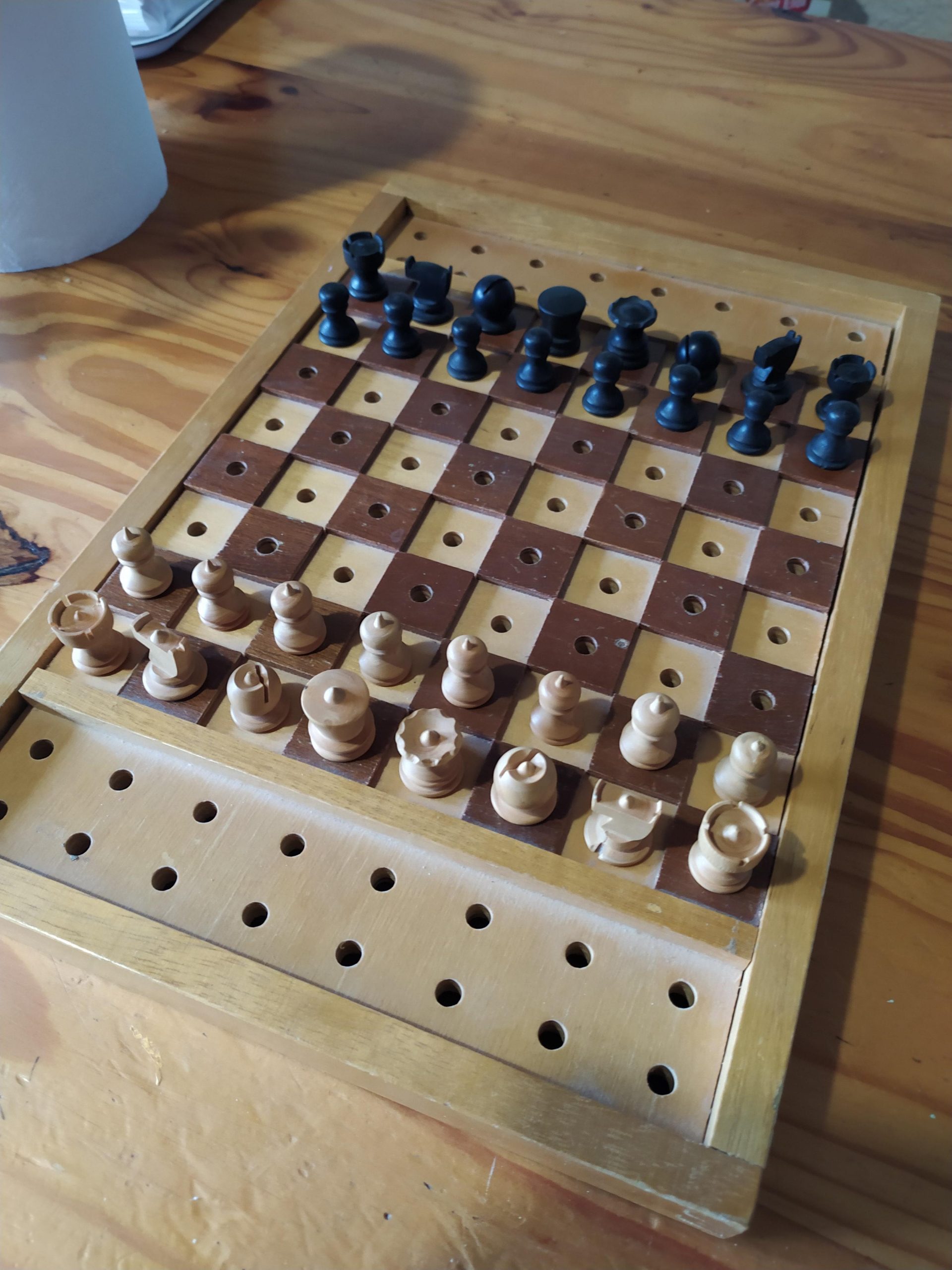Peg-style wooden chessboard with black and white pieces in starting position on a wooden table