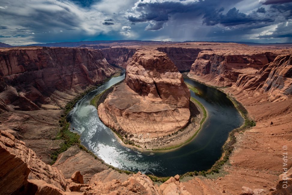 Horseshoe Bend mit einem geschwungenen Fluss, umgeben von hohen Felsen und Wolken am Himmel.