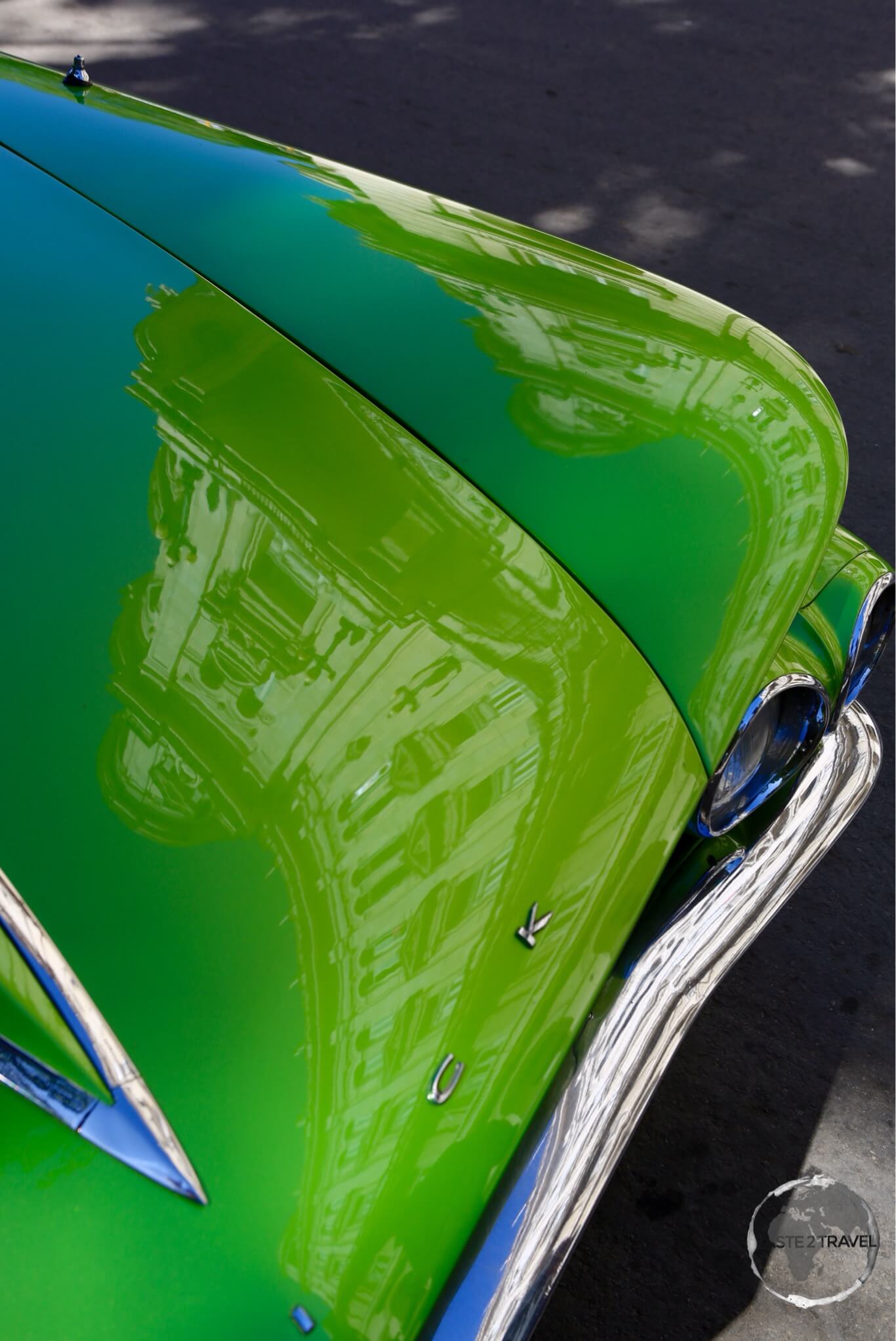 An ornate building in Havana old town is reflected off the polish hood of a Buick.