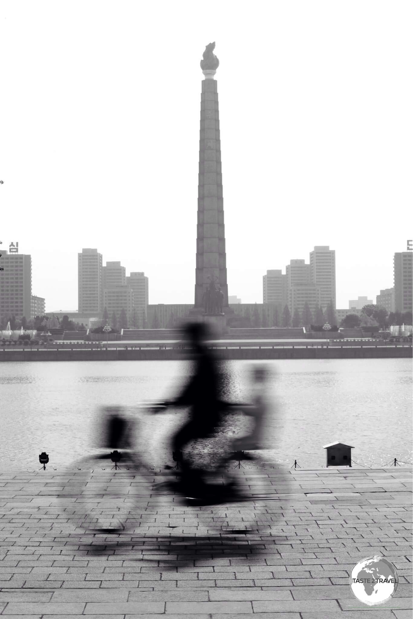 A cyclist on Kim Il-sung square, passing in front of Juche tower.