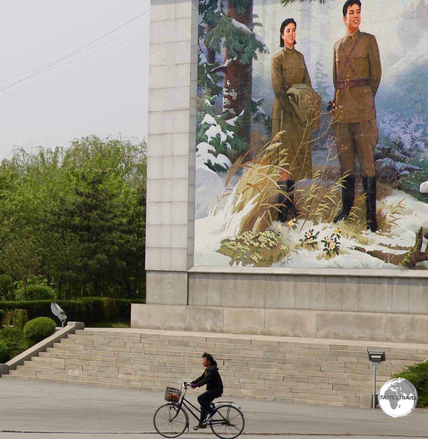 A cyclist in Nampo passes in front of a giant propaganda image.