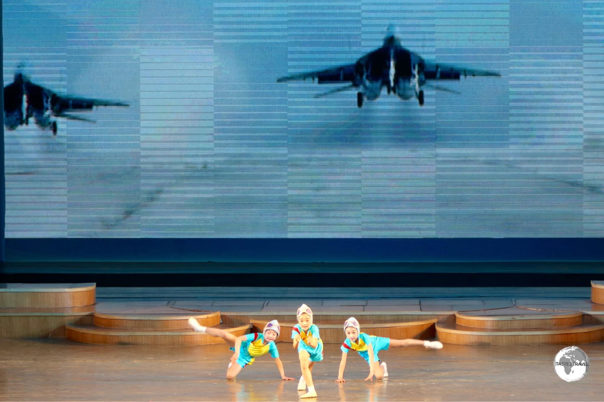 Girls at the Mangyongdae Schoolchildren’s Palace in Pyongyang, performing a choreographed <i>flight</i> routine in front of a screen displaying North Korean fighter jets.