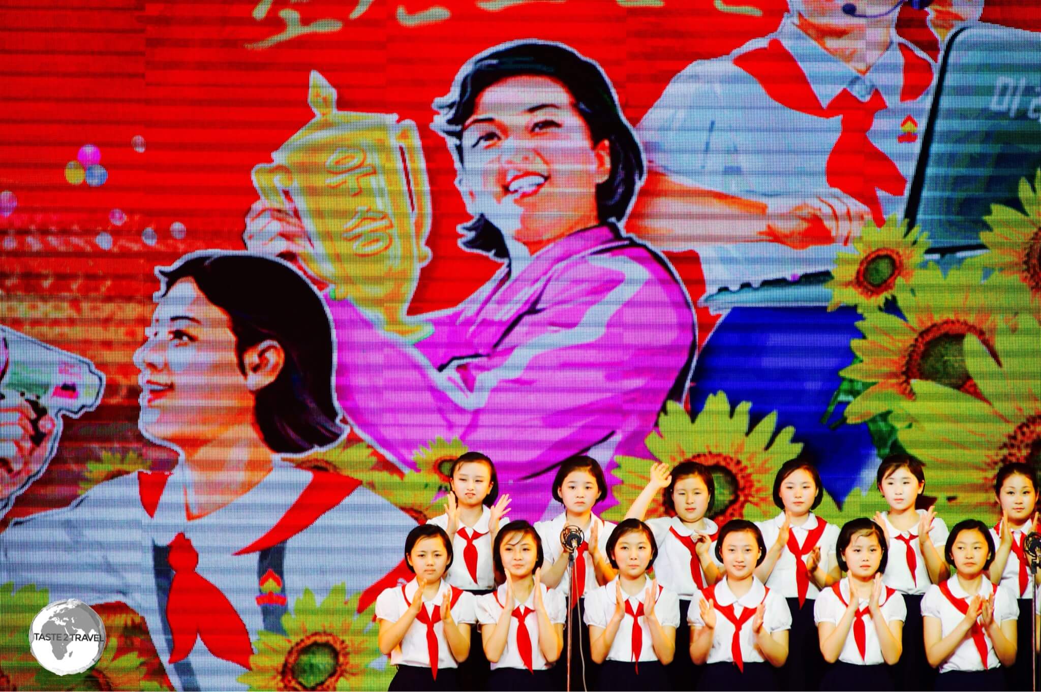 A girls choir at Mangyongdae Schoolchildren’s Palace performs in front of a propaganda poster.