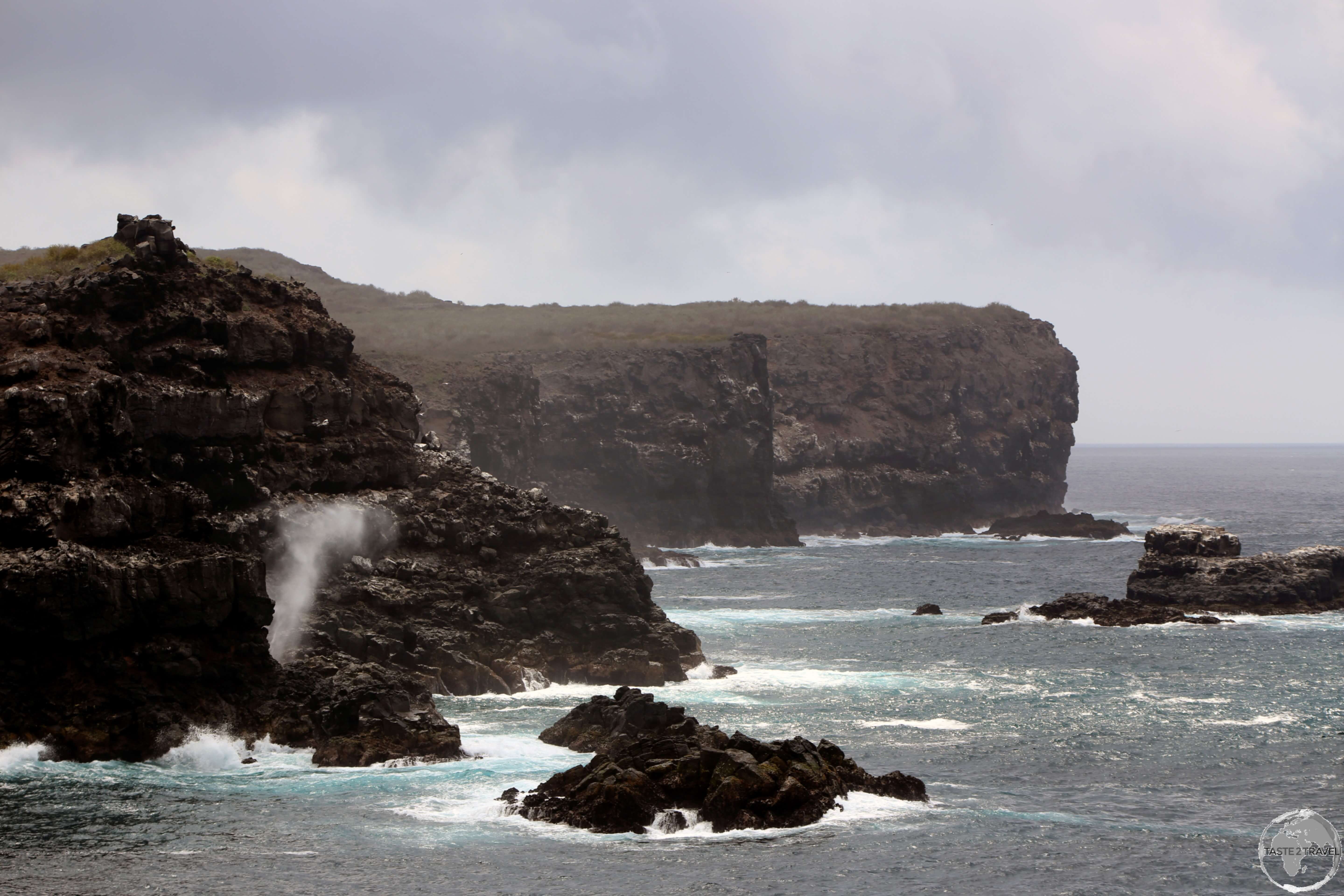 A view of the rugged coastline of Española Island with a smaller blow hole in the distance. 