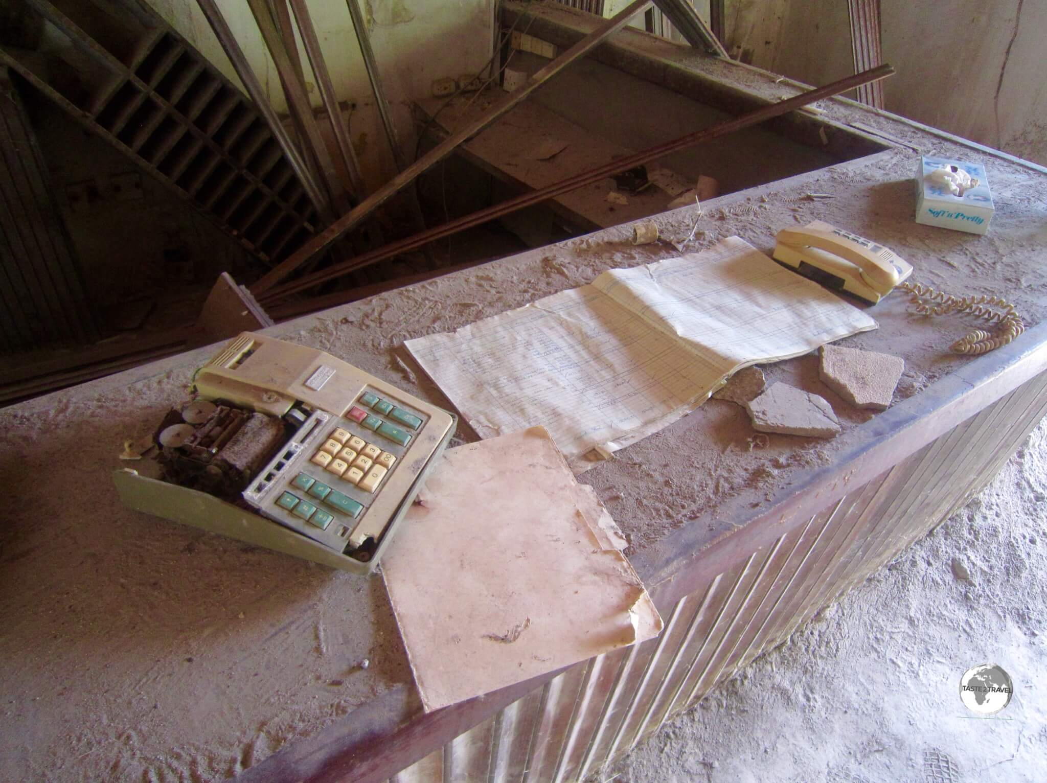 A calculator and ledger book remain on the reception desk of the abandoned Montserrat Springs Hotel.