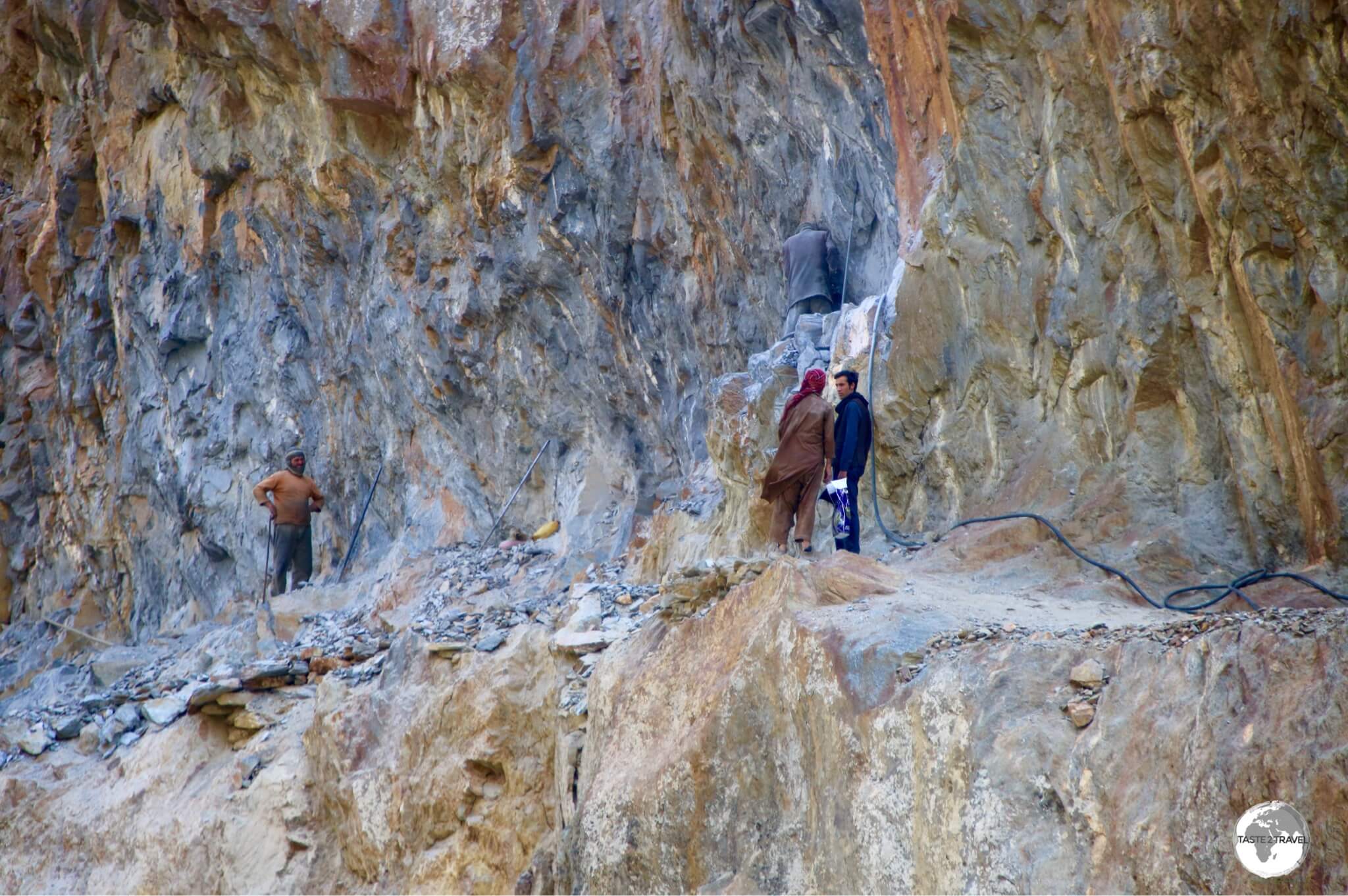 Afghan road workers carving the road out of a cliff face using a single jackhammer.