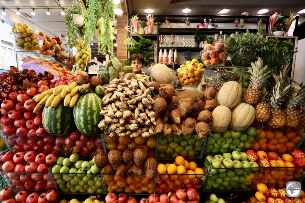 A vendor at a fruit juice shop, hidden by a wall of fruit, in Sulaimaniyah souk.